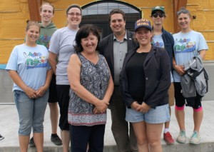 Photo : Jacinthe Laliberté ; Mme Laroche, la mairesse et le député David Graham entourés d’un groupe de moniteurs du camp Magicoparc posant devant le centre communautaire en rénovation.